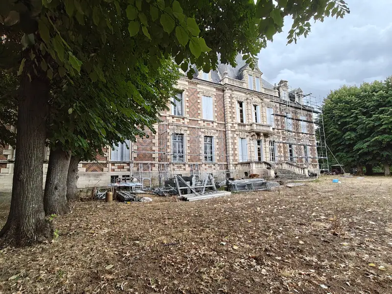 The brick facade glimpsed through the trees above a leaf-strewn slope