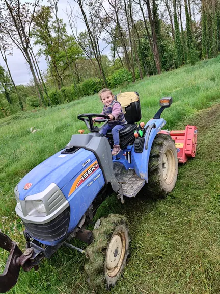 A child sitting at the wheel of the small blue estate tractor