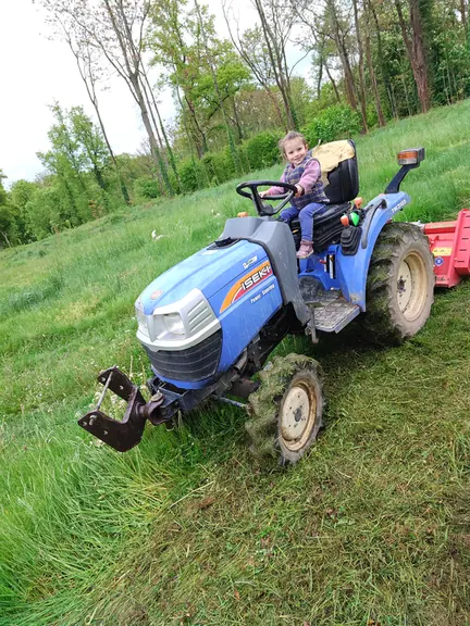 A child at the wheel of the tractor in the long grass