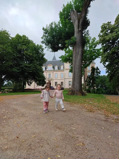 Two small girls running hand in hand along the drive towards the chateau