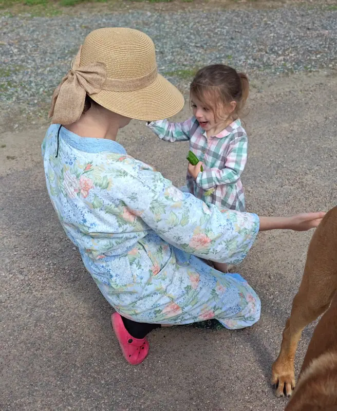 A mother in a sun hat crouching to talk with her small daughter, the family dog alongside