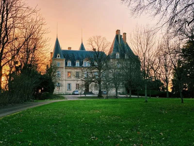 The chateau silhouetted against an orange sunset across the lawn